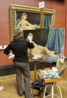 a woman standing in front of an easel with a painting on it's side