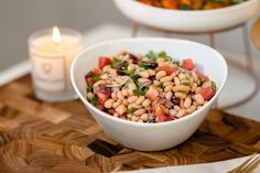 a white bowl filled with beans and veggies next to a candle