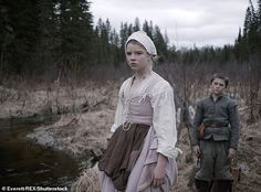 two people dressed in period clothing standing next to a stream and trees on the other side