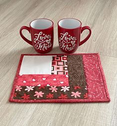 two coffee mugs sitting next to each other on top of a wooden table covered in fabric