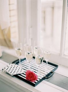 a tray with four champagne glasses and a rose on it next to a window sill