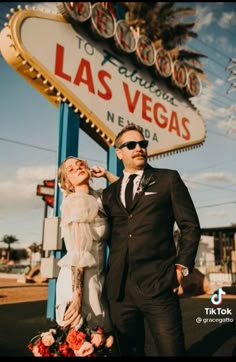 a man and woman standing in front of the las vegas sign