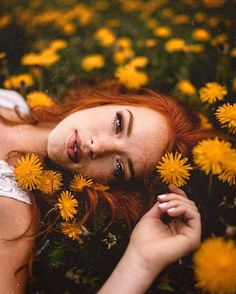 a woman laying in the grass surrounded by yellow dandelions and looking at the camera