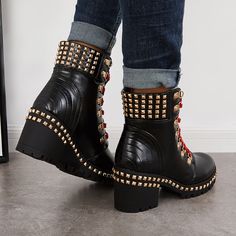 a pair of black boots with gold rivets and chains on the side, standing in front of a white wall