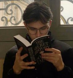 a man is reading a book in front of a window and looking down at it