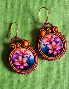 two earrings with flowers painted on them sitting on a green cloth covered surface, next to each other