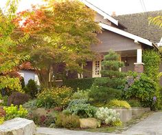 a house with lots of trees and plants in front of it, next to a sidewalk