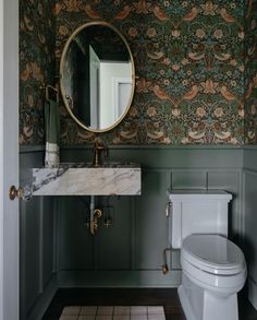 a white toilet sitting next to a bathroom sink under a round mirror on a wall