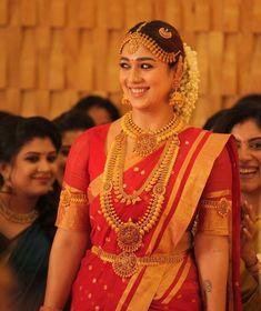 a woman in a red and gold sari smiles as she walks down the aisle