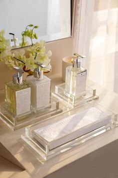 two square glass containers with perfume bottles on a table next to a mirror and flowers