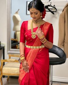 a woman in a red sari with gold jewelry on her neck and hands clasped