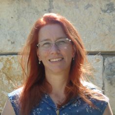 a woman with red hair and glasses is smiling at the camera while standing in front of a stone wall