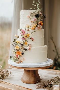 a white wedding cake with flowers on it sitting on a wooden table in front of a window