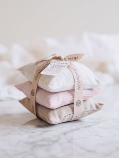 three pillows stacked on top of each other in front of a white bed with a pink ribbon