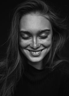 a smiling woman with freckles on her face and long hair is looking at the camera