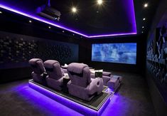 an empty theater room with purple lighting and recliners on the floor in front of a large screen