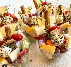 several small bowls filled with different types of appetizers and cheeses on skewers