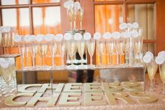 champagne glasses are lined up on a table with the word cheers spelled in gold letters