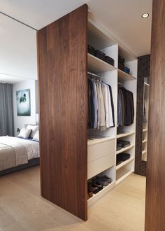 an open closet with clothes and shoes on shelves next to a bed in a bedroom