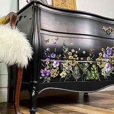 an ornate black dresser with flowers painted on it's sides and a white fluffy chair