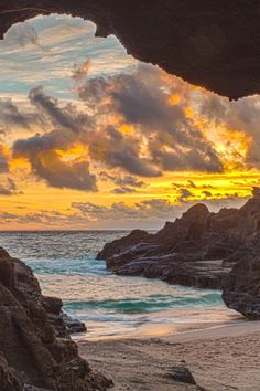 the sun is setting over the ocean from inside a cave on a beach with rocks and water