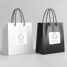 two black and white shopping bags with labels on the handles, one has a monogrammed wreath