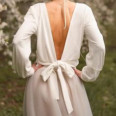 the back of a woman's white dress with long sleeves and a bow at the waist