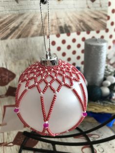 a red and white ornament hanging from a wire on a table next to yarn