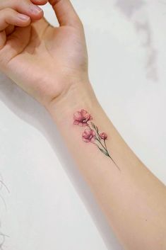 a woman's arm with a small pink flower tattoo on the left side of her wrist