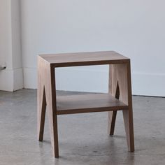 a small wooden table sitting on top of a cement floor next to a white wall