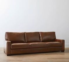 a brown leather couch sitting on top of a hard wood floor next to a white wall