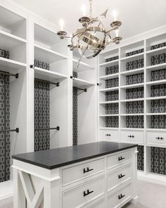 a walk in closet with white cabinets and black counter top, chandelier hanging from the ceiling