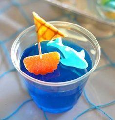 there is a small cup with blue liquid and an orange sail on it