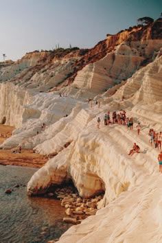 many people are standing on the edge of a cliff by the water and sand cliffs