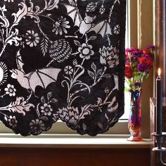 a black and white lace curtain hanging in front of a window with flowers on it