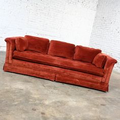 a red couch sitting on top of a cement floor next to a white brick wall