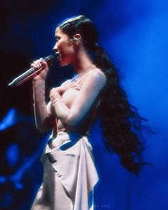 a woman with long black hair holding a microphone in her right hand and wearing a white dress