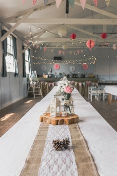 a long table with white linens and pine cones on the top, along with paper lanterns