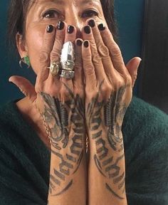 a woman covering her face with both hands and looking at the camera while wearing tattoos