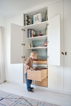 a little boy standing in front of a drawer with books on it's shelves