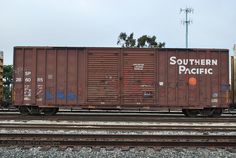 a train car sitting on the tracks with graffiti painted on it's side and another boxcar in the background