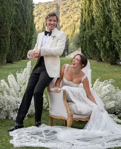 a woman in a wedding dress sitting on a chair next to a man in a tuxedo