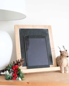 a tablet sitting on top of a wooden shelf next to a christmas wreath and pine cones