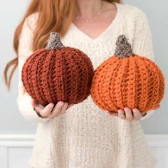 two crocheted pumpkins are shown in front of a woman's face