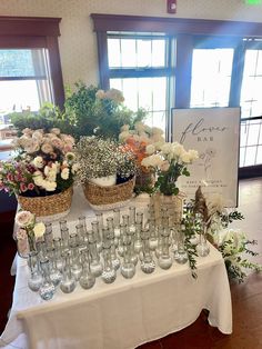 a table topped with lots of glasses filled with flowers and greenery next to a sign