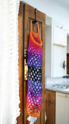 a colorful bag hanging on a door handle in a kitchen with white lace and wood cabinets