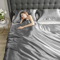 a woman laying on top of a bed covered in silver sheets and pillows with her head resting on the pillow