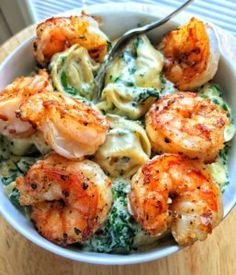 a bowl filled with pasta and shrimp on top of a wooden table next to a fork