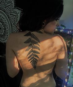 the back of a woman's body with a fern tattoo on her left side