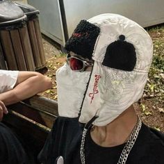 a person wearing a white mask and black hat with chains around his neck sitting on a bench